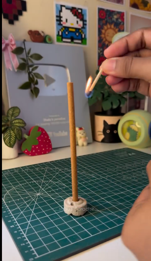Hand opening a Zoura Parfums premium bakhoor stick jar, Oud Amber scent, on a desk workspace setting.