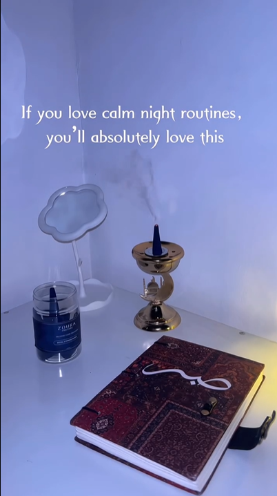 Hand holding a blue Zoura Parfums bakhoor cone over its jar, warm woody calming incense fragrance.