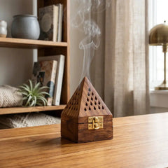 Wooden bakhoor burner emitting smoke on a wooden surface with a bookshelf in the background
