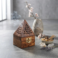 Wooden bakhoor burner with smoke, flowers, and crystals on a gray surface