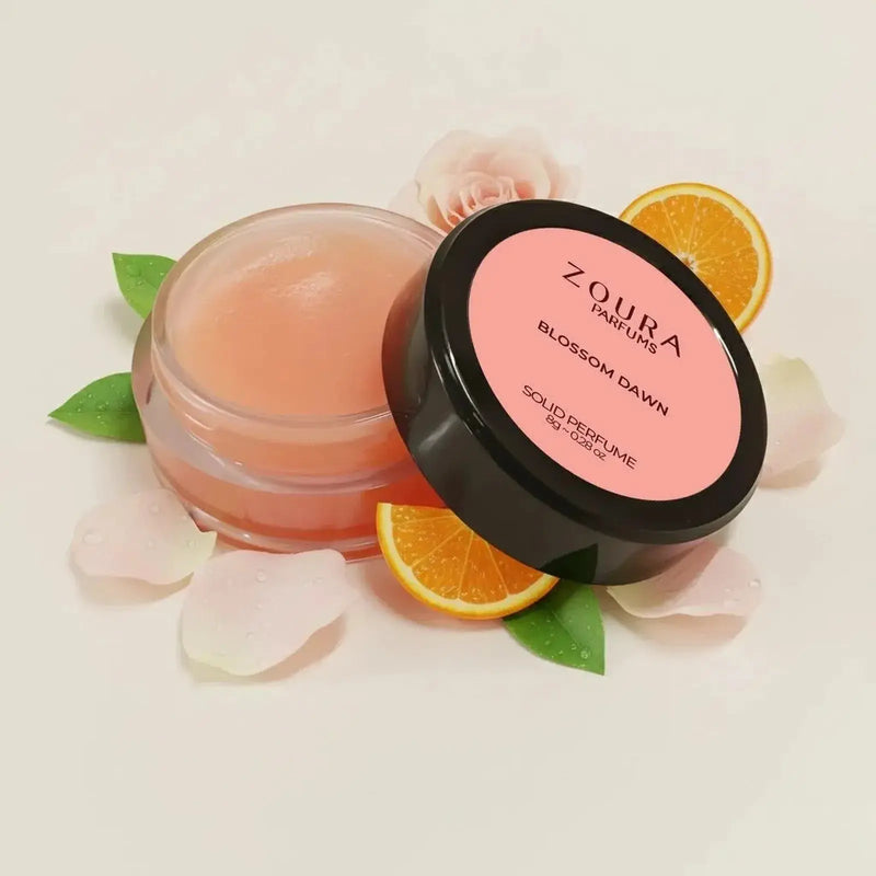 Open jar of Zoura Blossom Dawn Luxury Solid Perfume with rose petals and orange slices