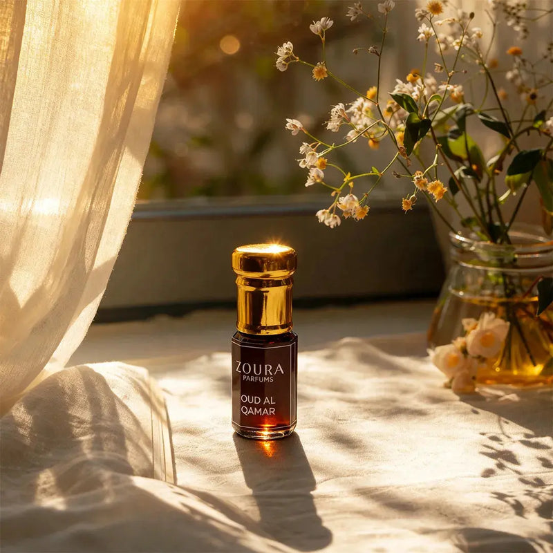 Zoura Parfums Oud Al Qamar attar bottle on linen in warm sunlit window light with wildflowers